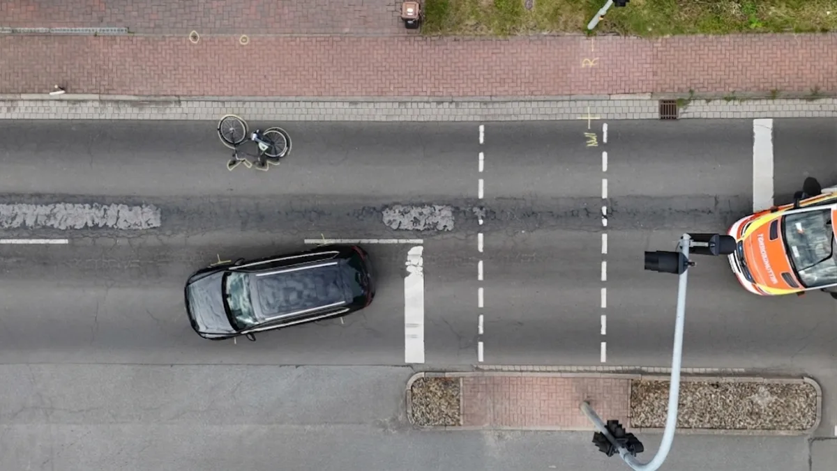 Ein schwarzes Auto steht auf der Straße, neben einem umgekippten Fahrrad. Ein Rettungswagen ist ebenfalls anwesend.