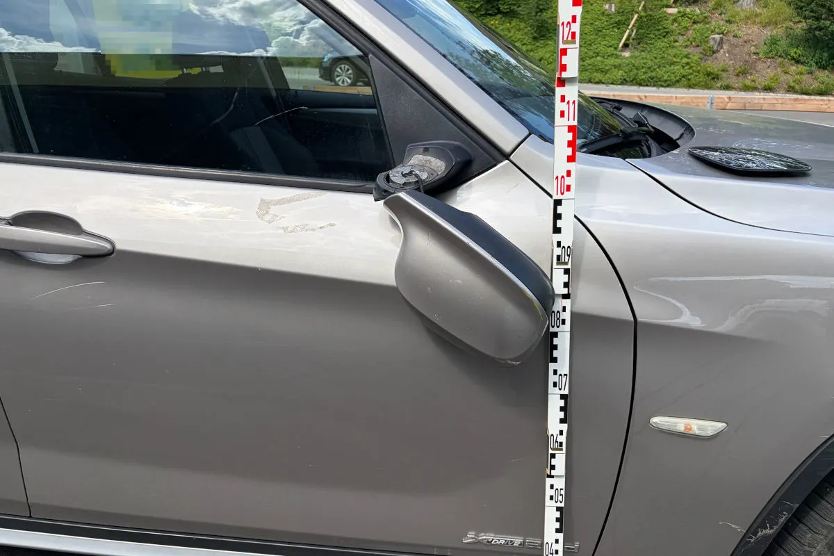 Ein graues Auto mit einem beschädigten Seitenspiegel; daneben steht ein Maßstab zur Messung.