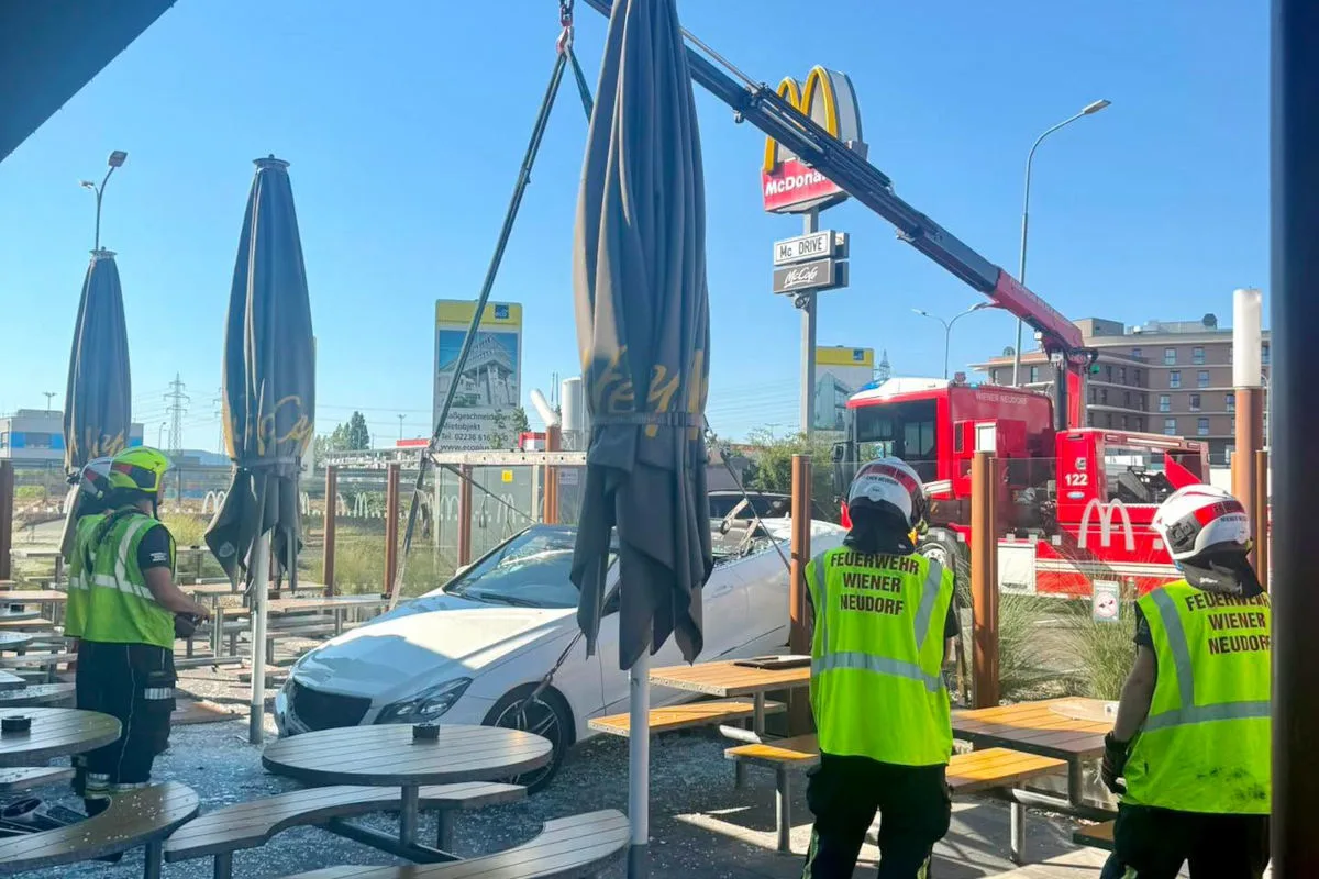 Ein weißes Auto steht im Außenbereich eines Fast-Food-Restaurants; Feuerwehrleute sind anwesend und sichern die Szene.