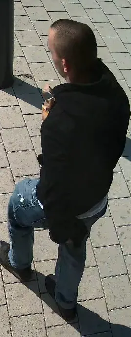 Ein Mann in dunkler Kleidung, von hinten aufgenommen, geht auf einem gepflasterten Gehweg.