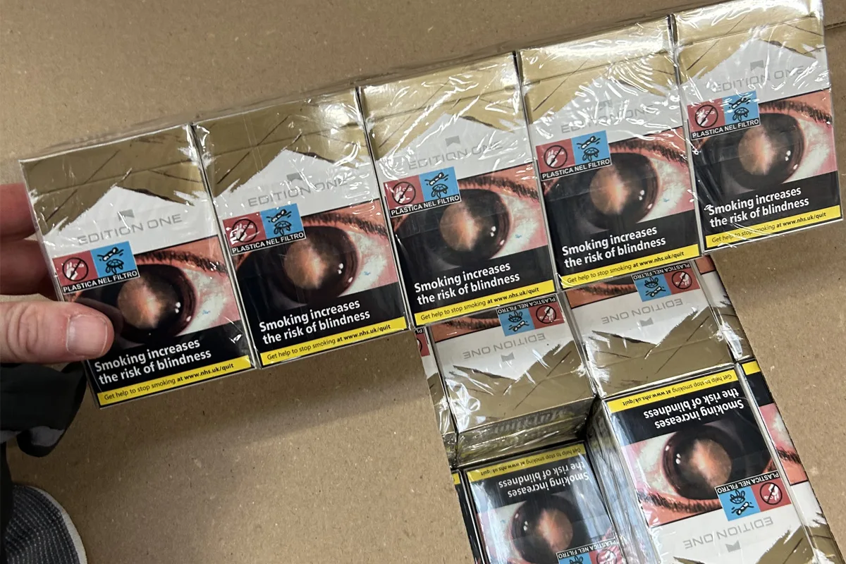 Mehrere Zigarettenschachteln sind sichtbar, jede trägt einen Aufdruck mit einem großen Auge und einer Warnung vor Blindheit.