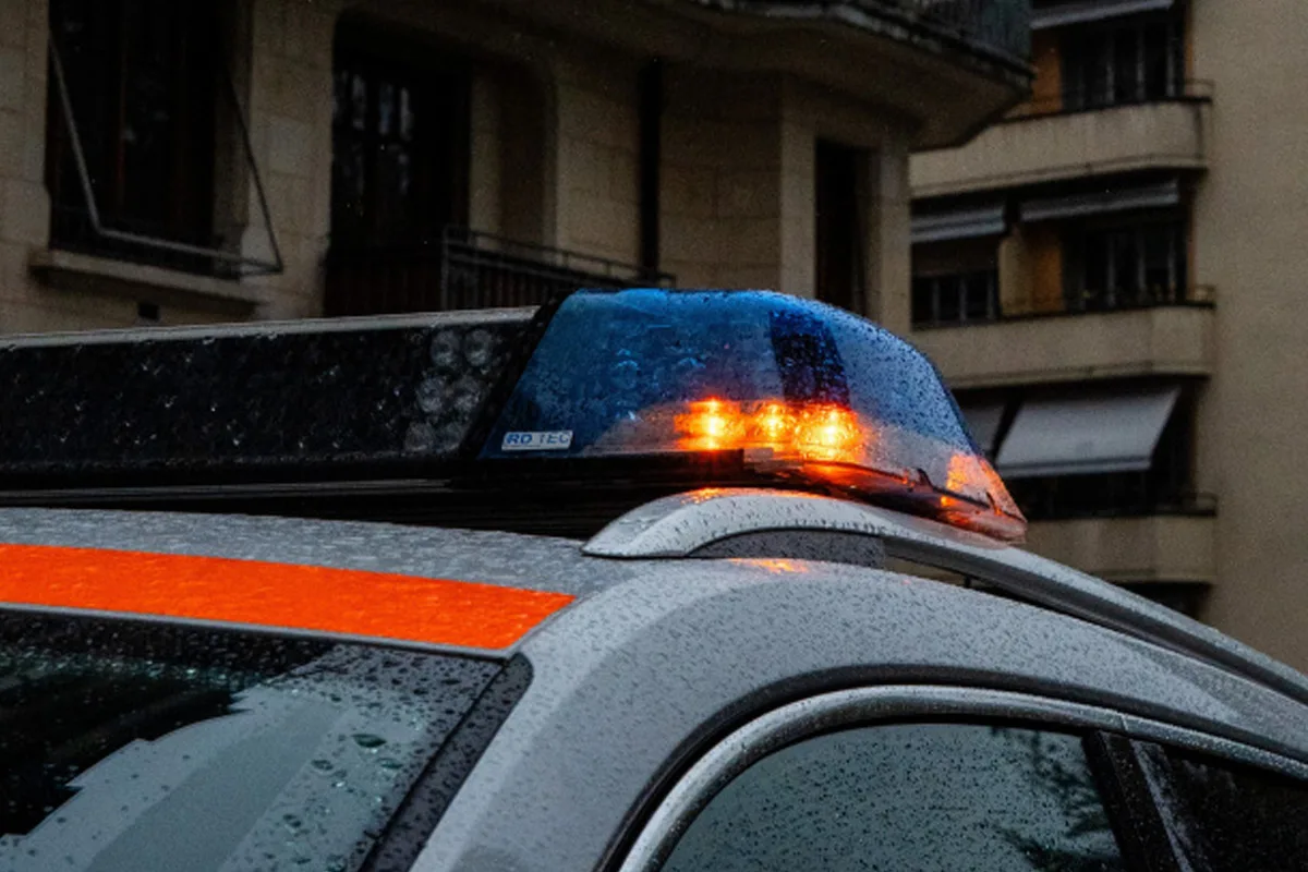 Ein Polizeifahrzeug mit eingeschaltetem Blaulicht steht im Regen. Im Hintergrund sind mehrstöckige Gebäude.