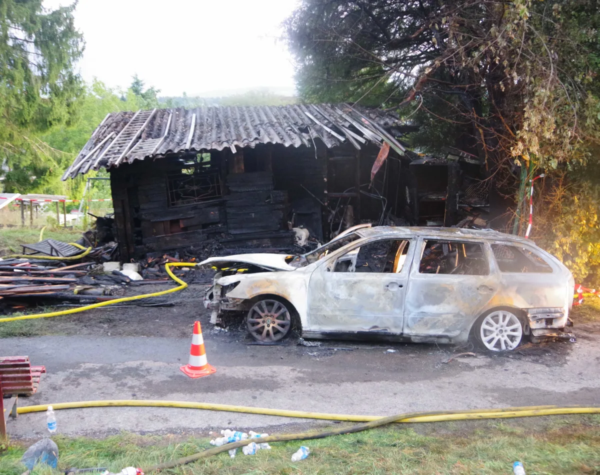 Ein ausgebranntes Auto steht vor einem ebenfalls zerstörten Gebäude. Im Vordergrund liegen Schläuche und eine Warnbake.