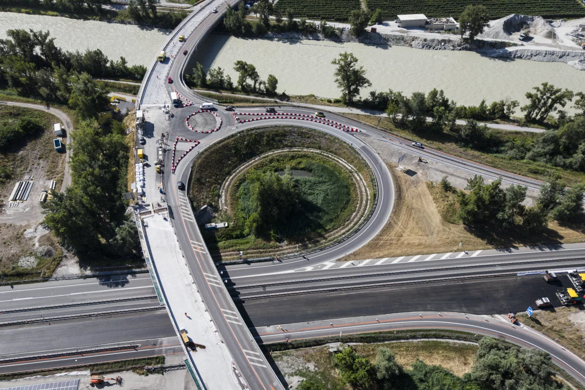 Die Luftaufnahme zeigt eine im Bau befindliche Überführung mit klarer Straßenführung und Baustellenfahrzeugen auf einer mehrspurigen Straße.
