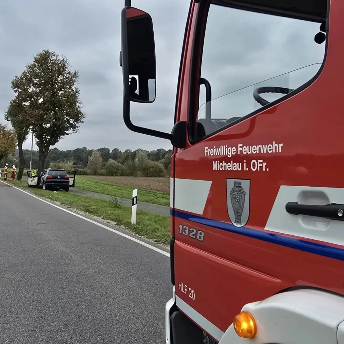 Ein Feuerwehrauto der Freiwilligen Feuerwehr Michelau i. OFr. steht am Straßenrand, im Hintergrund ein Pkw an einem Baum.