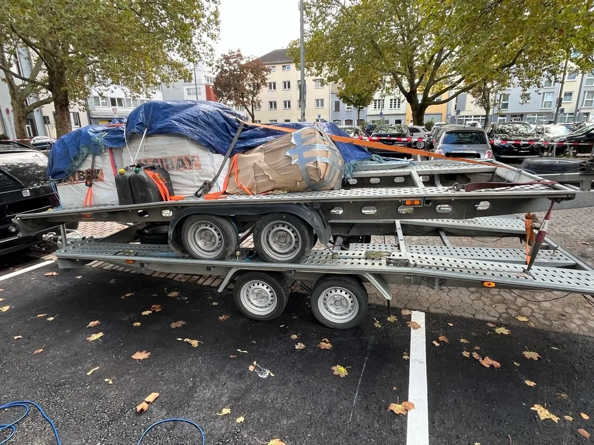 Ein großer Anhänger parkte auf einem Parkplatz, beladen mit mehreren verpackten und mit Planen abgedeckten Gegenständen.