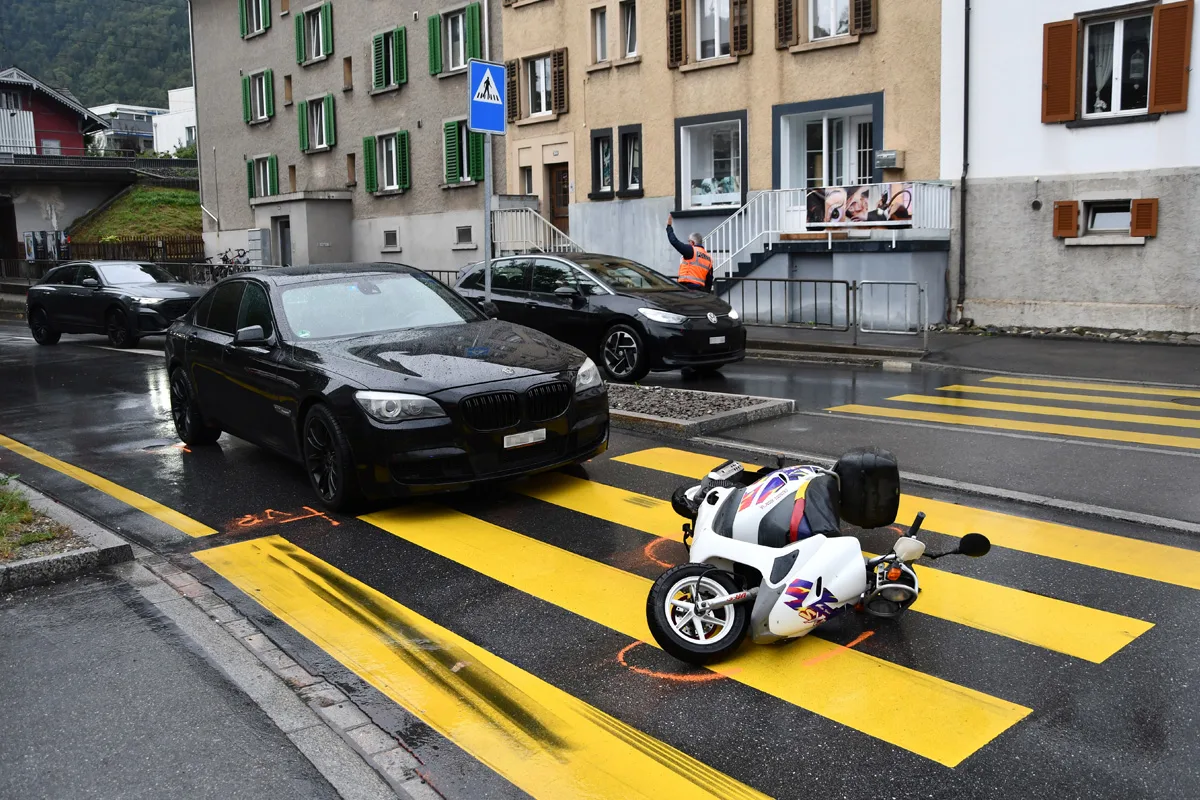 Auf einem Zebrastreifen liegt ein umgestürztes Pocketbike neben einem schwarzen BMW. Ein Mann im orangefarbenen Warnwesten dirigiert den Verkehr in der Nähe.