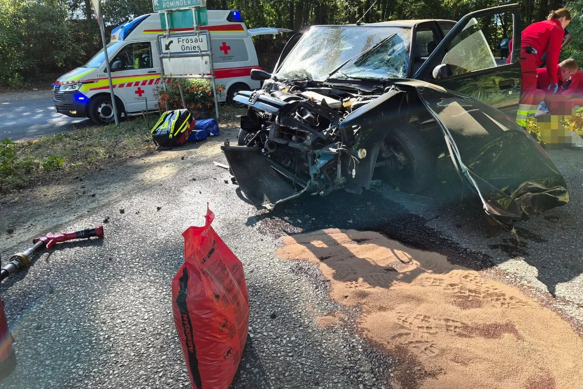 Ein stark beschädigtes Auto steht mit offener Tür auf der Straße. Im Hintergrund ist ein Krankenwagen zu sehen.