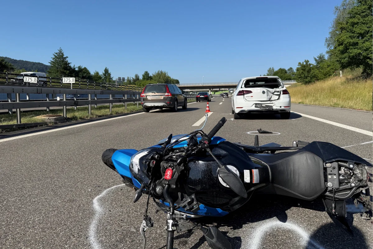 Ein blau-schwarzes Motorrad liegt umgestürzt auf der Autobahn. Im Hintergrund steht ein beschädigtes weißes Auto.