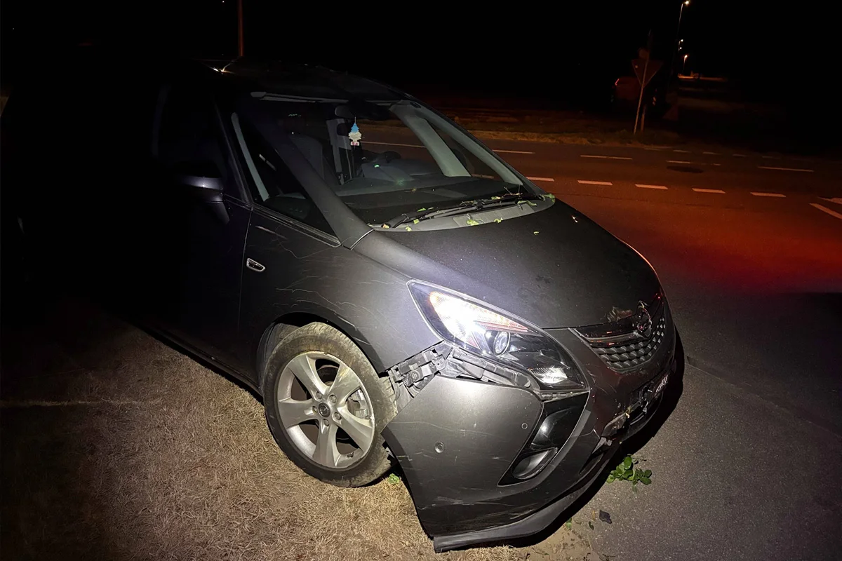 Ein silbernes Auto mit beschädigter Stoßstange steht bei Nacht am Straßenrand. Die Umgebung ist dunkel, nur der Wagen ist ausgeleuchtet.
