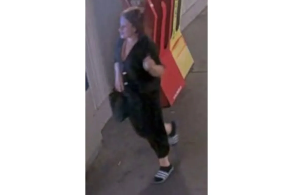 Eine Frau in dunkler Kleidung geht auf einem Gehweg, während sie an einem roten und gelben Aufsteller vorbeikommt.