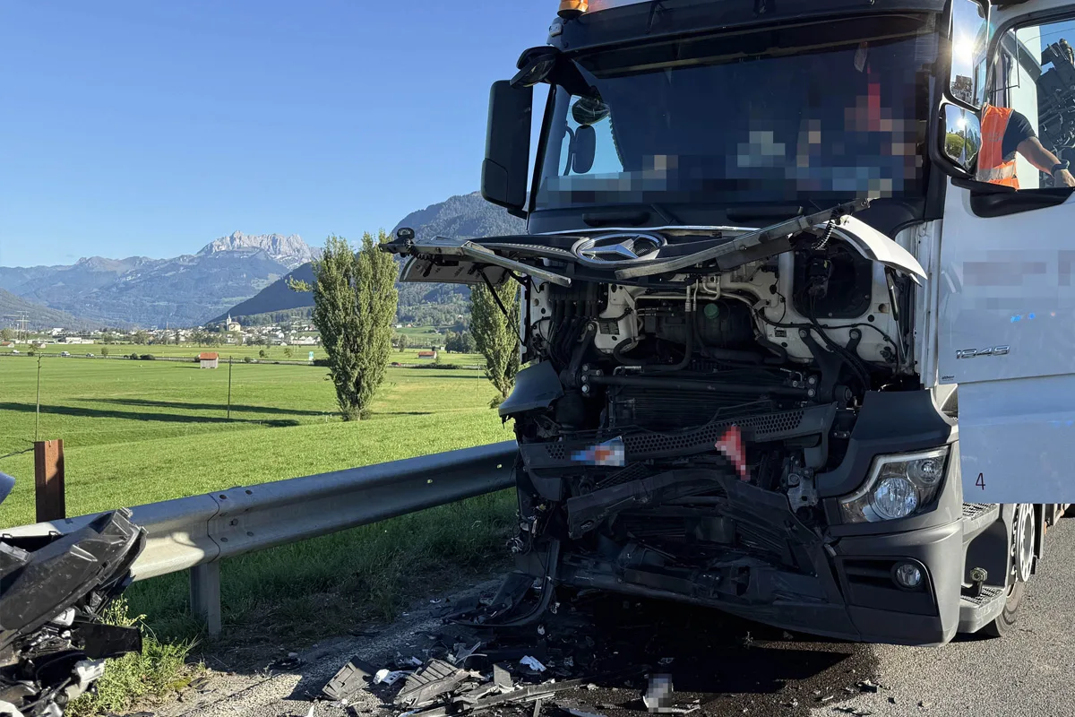 Ein Lastwagen mit schwerem Frontschaden steht auf einer Landstraße. Im Hintergrund sind Berge und eine grüne Landschaft sichtbar.