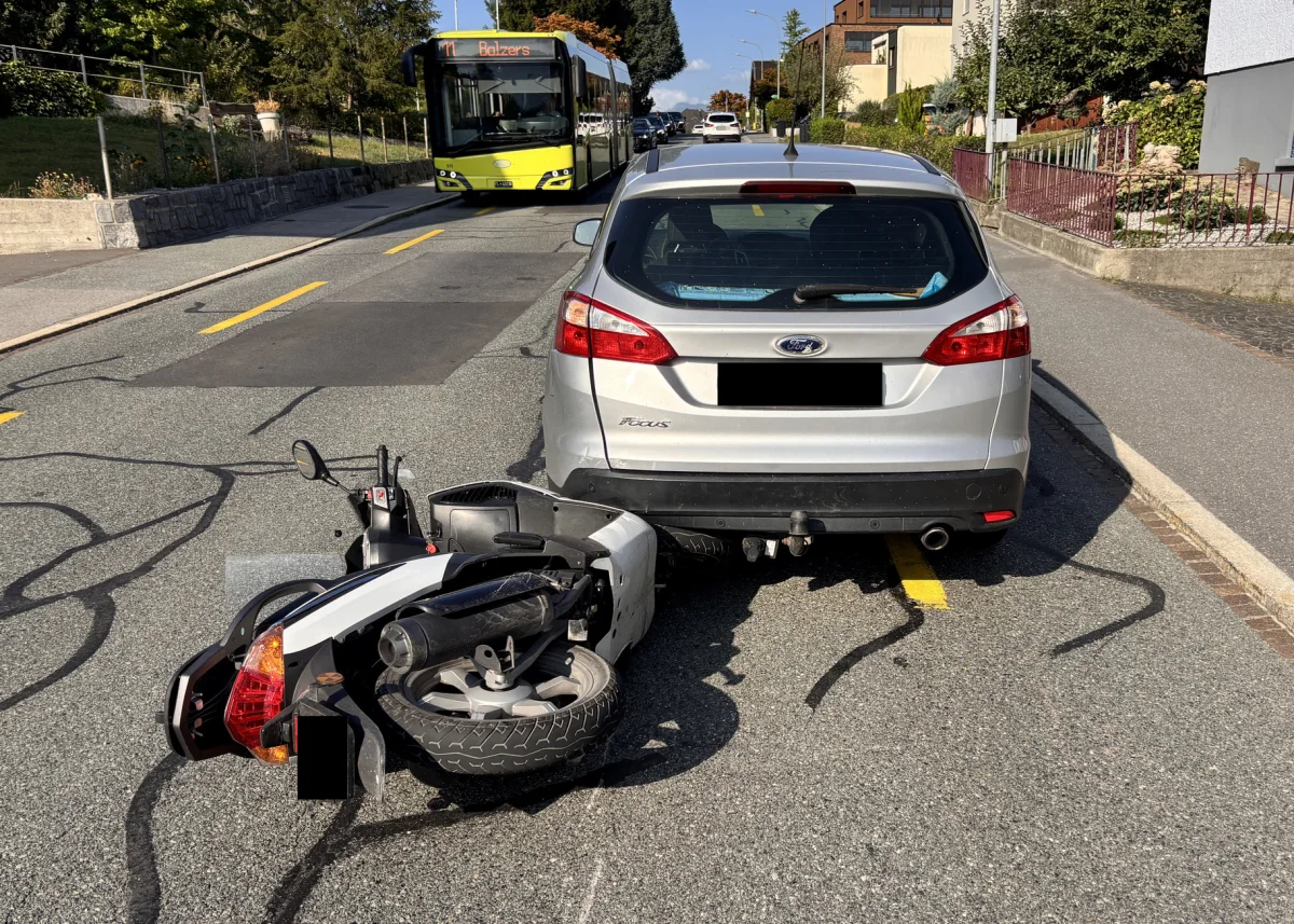 Ein umgekippter Roller liegt hinter einem silbernen Ford Focus auf der Straße. Im Hintergrund ist ein gelber Bus zu sehen.