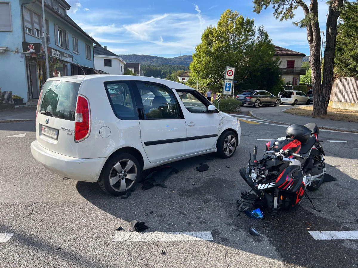 Ein weißes Auto mit Schäden an der Seite und ein stark beschädigtes Motorrad stehen nach einem Unfall auf einer asphaltierten Kreuzung.