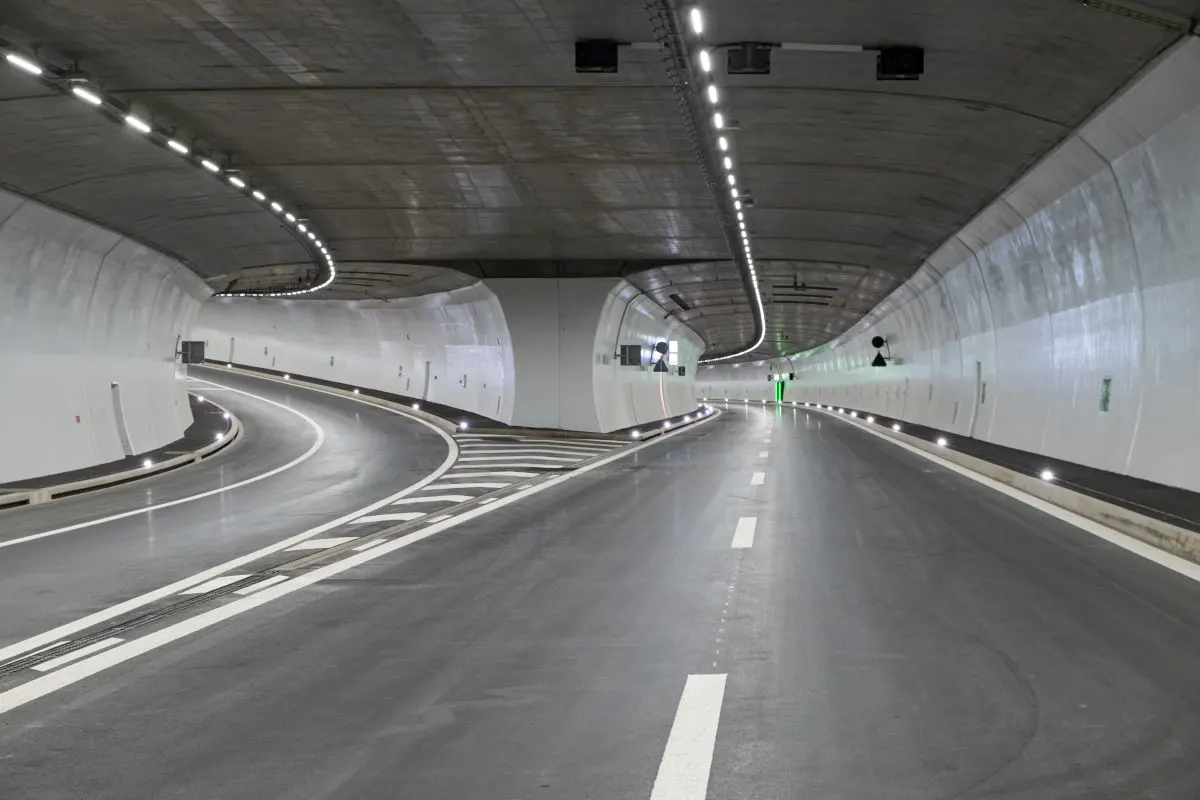 Ein leerer Straßentunnel ist zu sehen, der eine deutliche Kurve beschreibt. Der Tunnel ist gut beleuchtet, ohne Fahrzeuge.