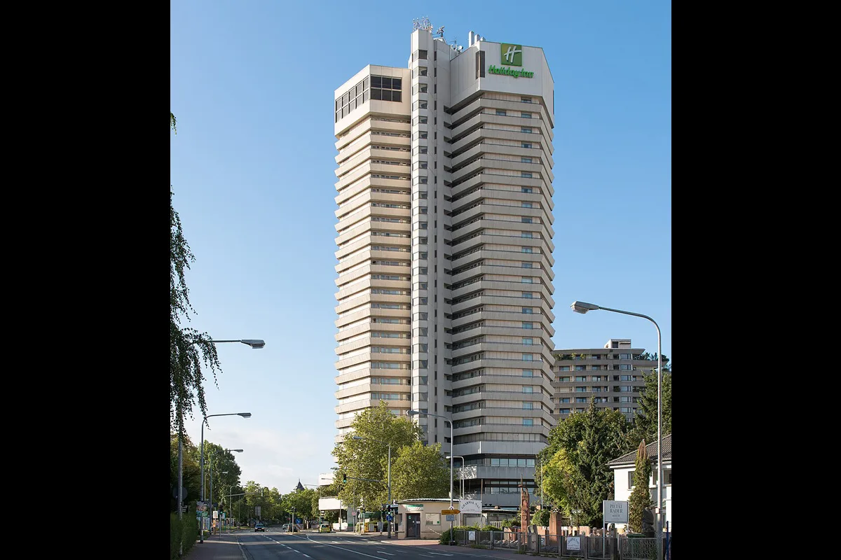 Das Bild zeigt ein hohes Hotelgebäude mit einem erkennbaren Logo oben. Der Himmel ist klar und blau.