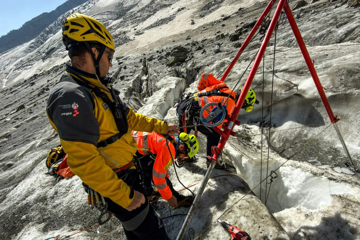 Eine Gruppe von Rettungskräften arbeitet an einer Gletscherspalte, ausgestattet mit Seilen und Schutzkleidung.