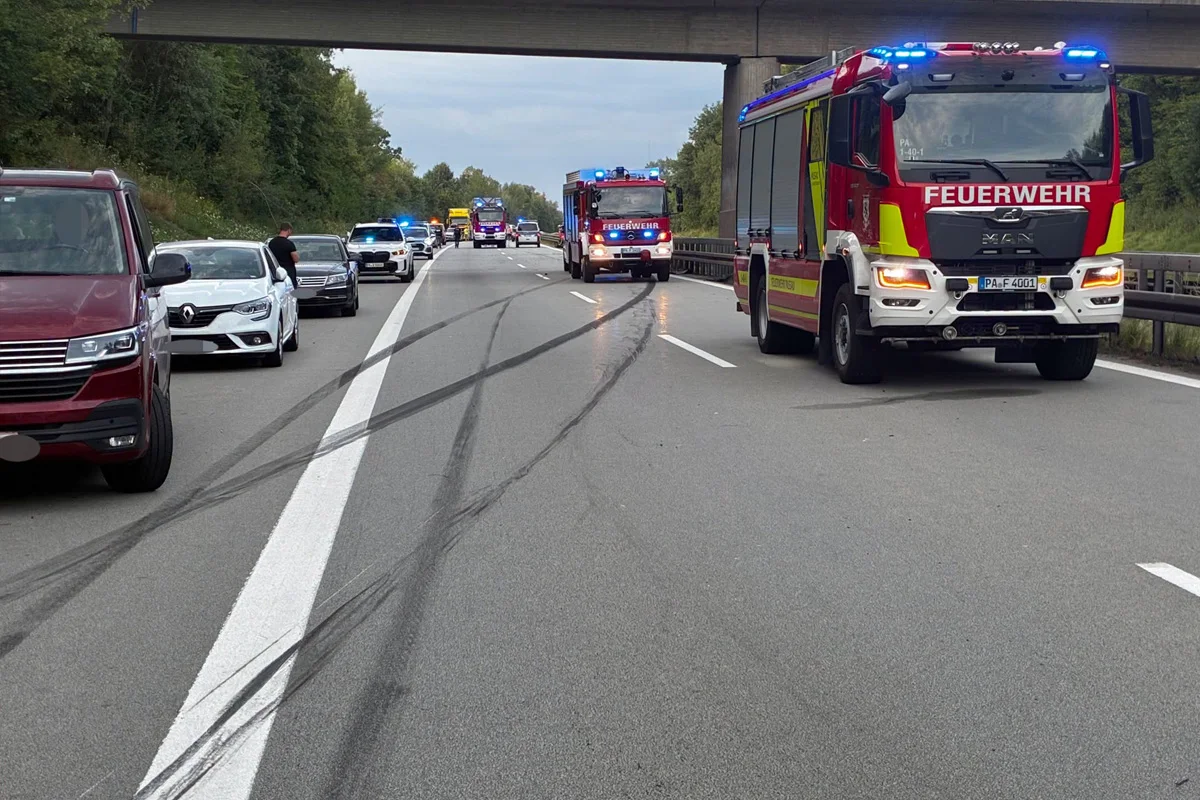 Mehrere Feuerwehr- und Polizeifahrzeuge sind auf einer zweispurigen Autobahn vor Ort, umgeben von abgestellten Fahrzeugen, bei wolkigem Wetter.