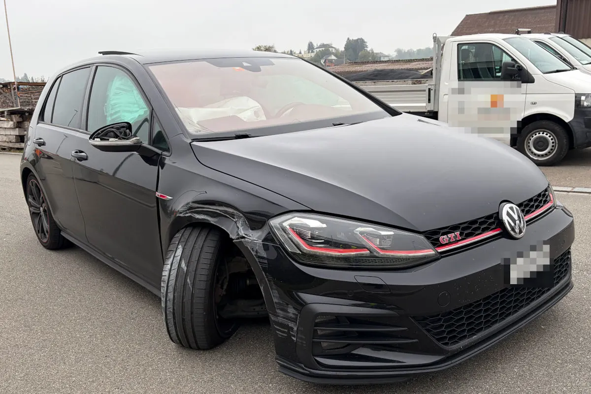 Ein schwarzer VW Golf mit sichtbaren Schäden am rechten Vorderreifen steht auf einer Straße. Ein weiteres Fahrzeug im Hintergrund.