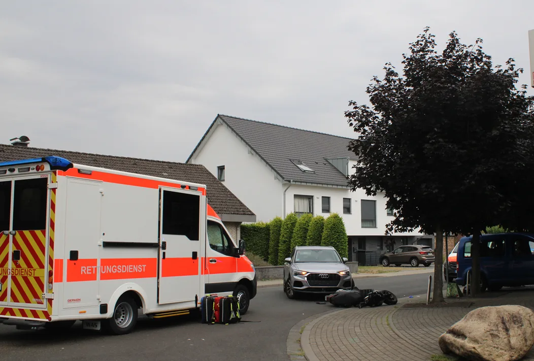 Ein Rettungswagen mit offenen Türen parkt in einem Wohngebiet, daneben mehrere Autos und Gepäck.