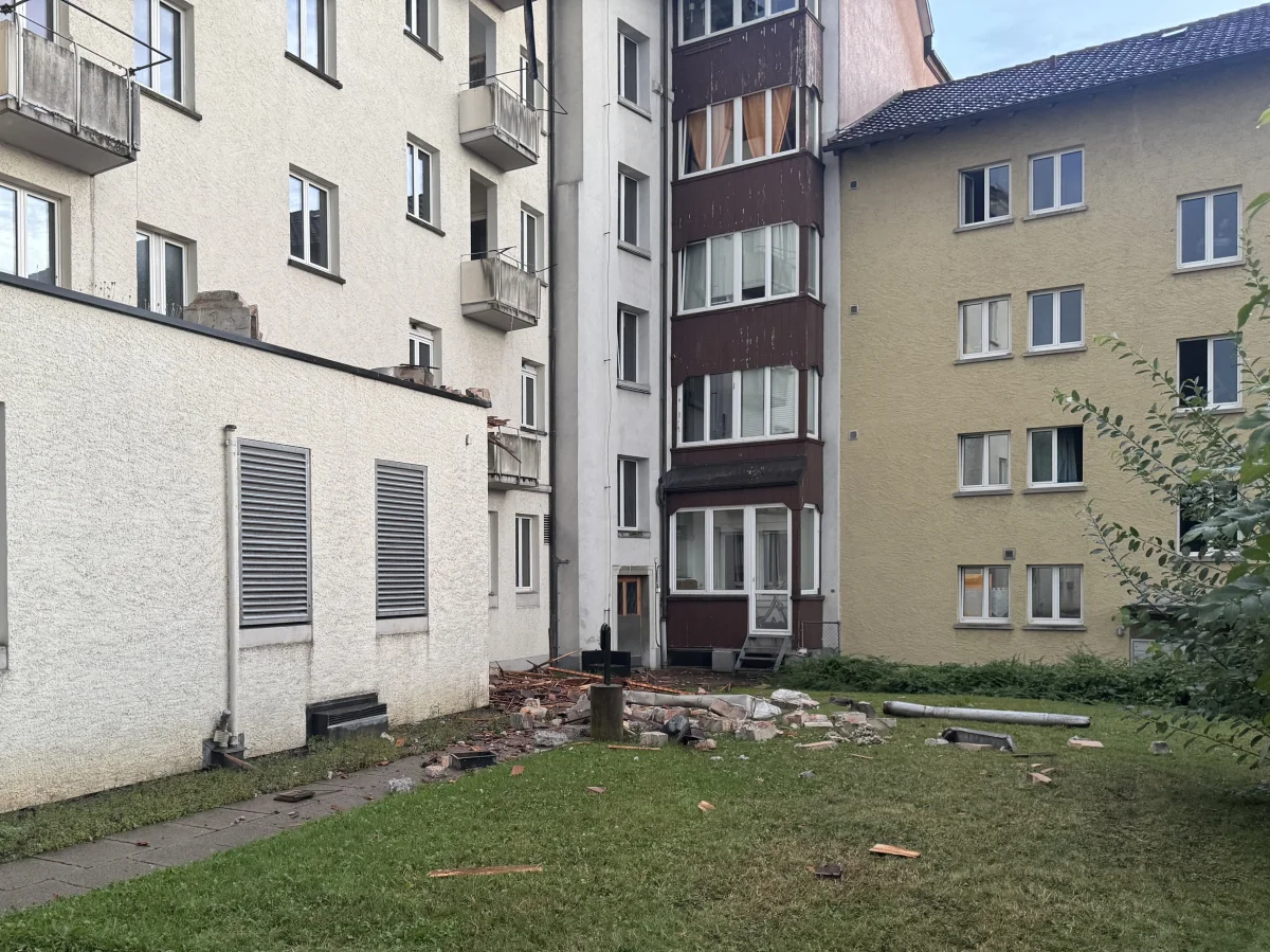 Im Innenhof eines Wohnhauses sind Mauertrümmer und Gebäudeschäden zu sehen. Der Rasen ist mit Steinen und Holzteilen übersät.