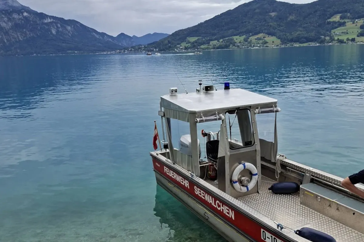 Ein Feuerwehrboot der Einheit Seewalchen liegt auf einem klaren See, im Hintergrund Berge und bewaldete Hügel.