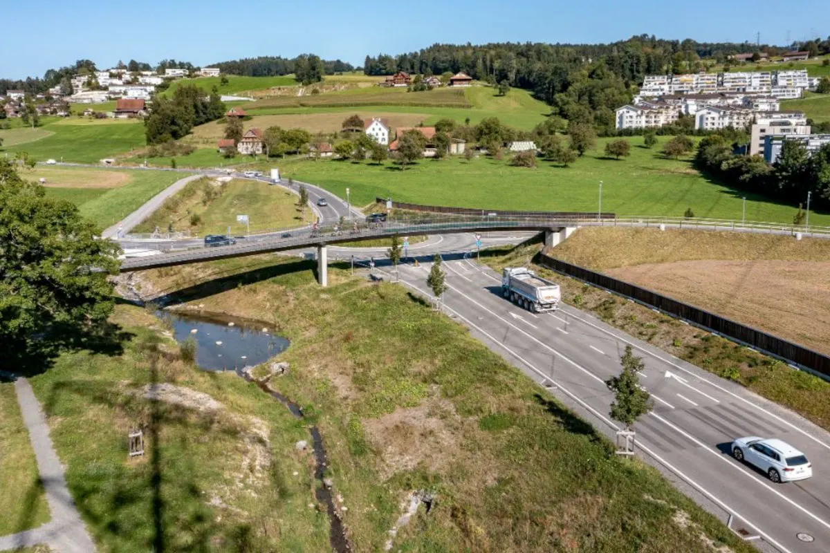 Eine Luftaufnahme zeigt eine Straßenkreuzung auf dem Land, eine Brücke und verschiedene Fahrzeuge bei leichtem Verkehr.