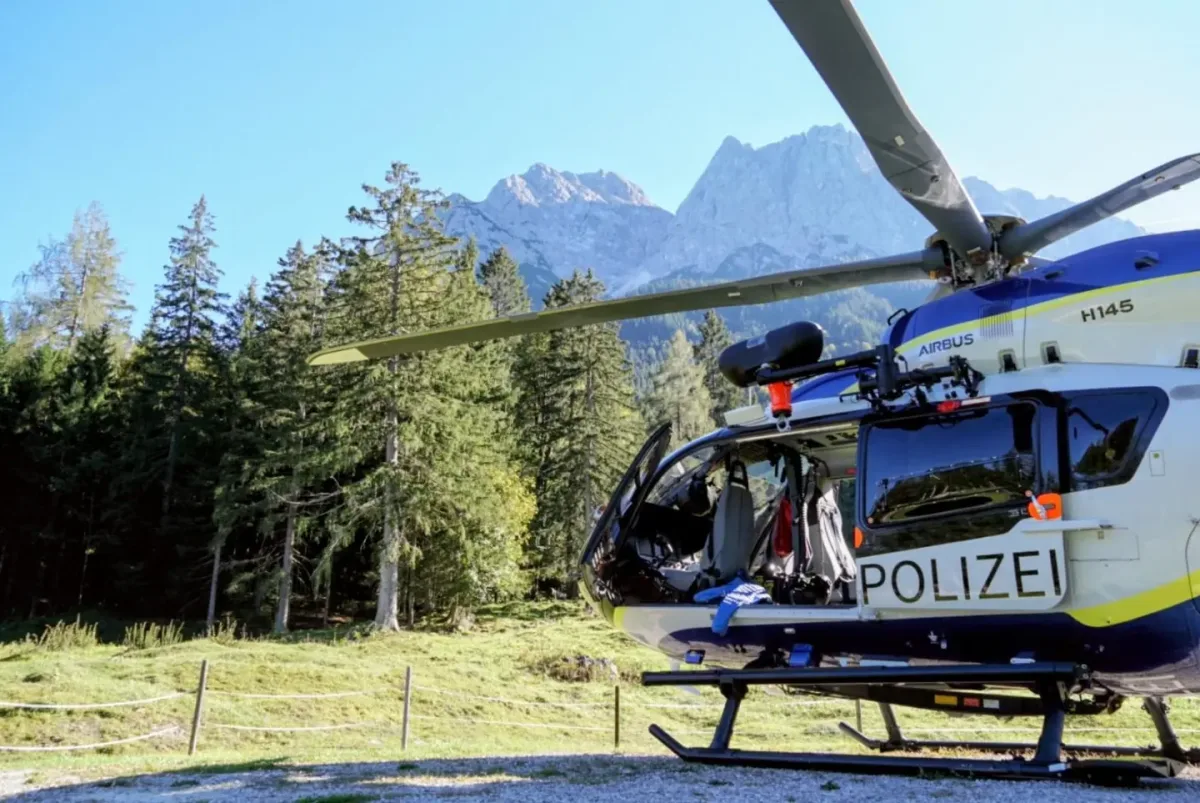 Ein Polizeihubschrauber vom Typ Airbus steht auf einer Lichtung, umgeben von Bäumen und Bergen. Die Tür des Hubschraubers ist geöffnet, und Ausrüstung ist sichtbar.