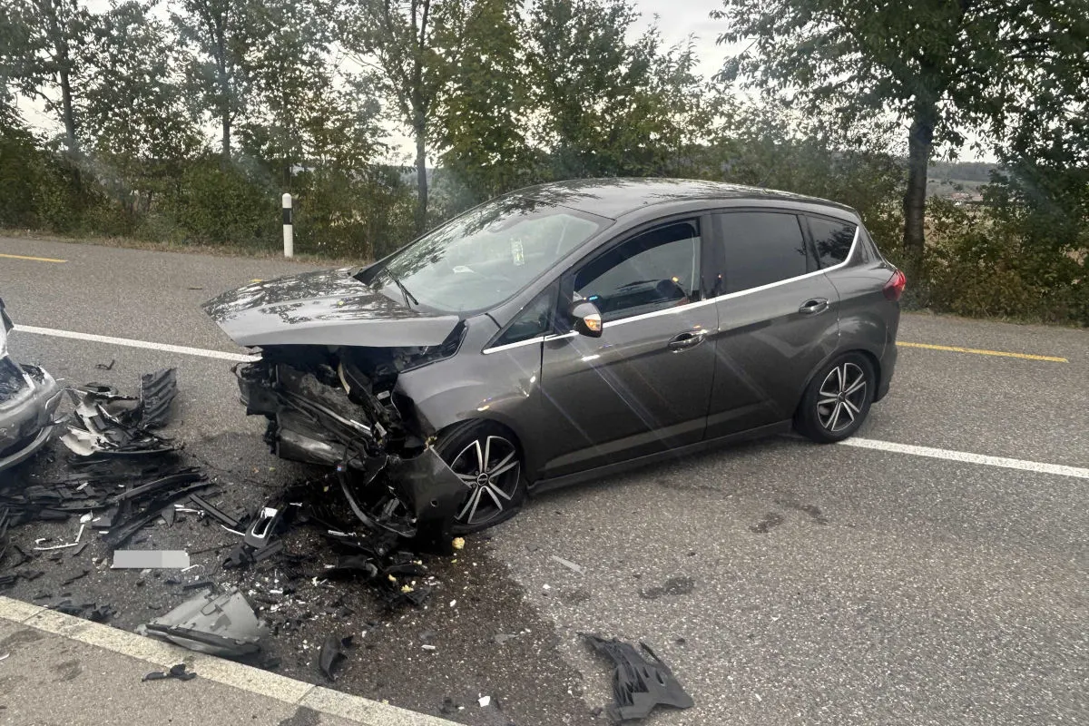 Ein graues Auto steht mit schwerem Frontschaden auf einer Landstraße. Trümmerteile liegen verstreut auf der Straße.