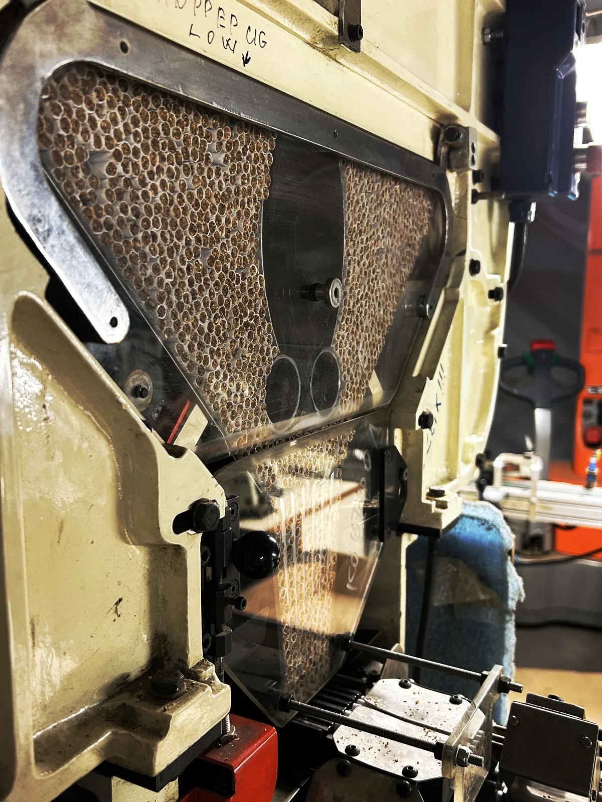 Eine technische Maschine mit metallischen und durchsichtigen Elementen ist in einer Fabrikumgebung zu sehen, wobei verschiedene mechanische Teile sichtbar sind.