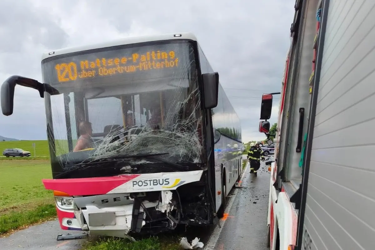 Ein Postbus mit erkennbar beschädigter Frontscheibe steht auf der Straße. Rettungskräfte sind im Hintergrund sichtbar.