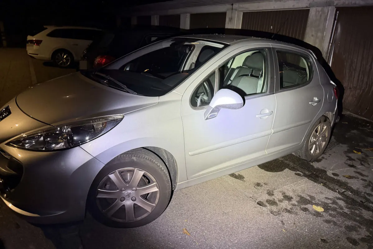 Ein silbernes Auto steht auf einem teilweise beleuchteten Parkplatz bei Nacht. Der Bereich ist dunkel mit einigen anderen Fahrzeugen.