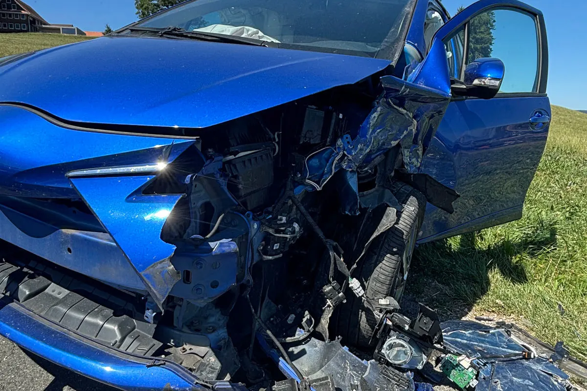 Nahaufnahme eines stark beschädigten blauen Autos. Die Front des Fahrzeugs ist eingedrückt und die Fahrertür steht offen.