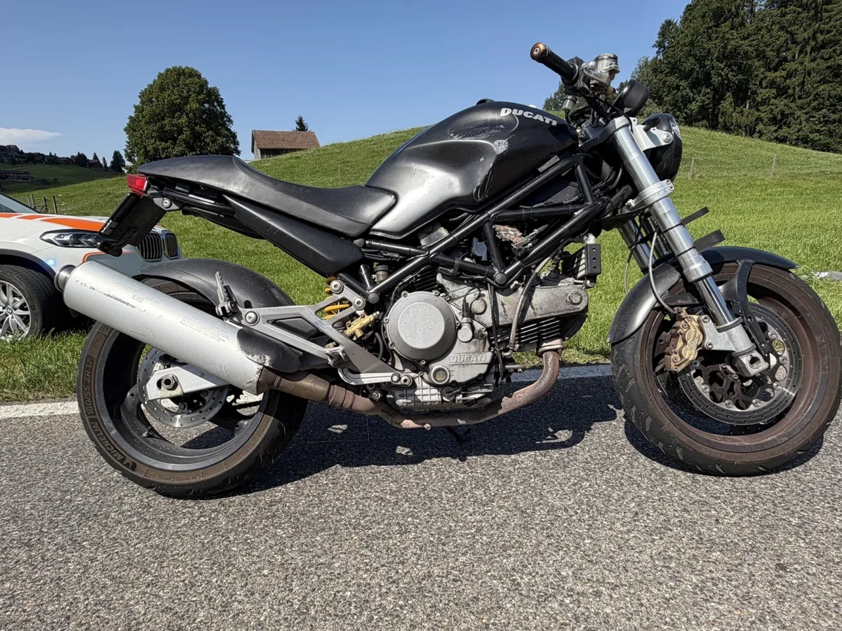 Ein schwarzes Motorrad steht auf einer Landstraße, daneben parkt ein Polizeiauto im Gras. Der Himmel ist klar.