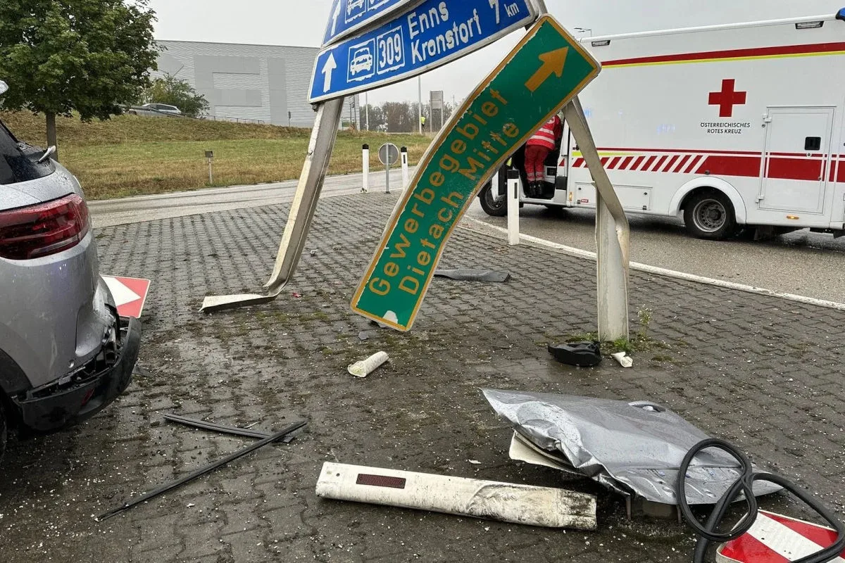 Ein stark beschädigtes Verkehrsschild steht schräg neben einem beschädigten Auto. Im Hintergrund ist ein Fahrzeug des Roten Kreuzes zu sehen.