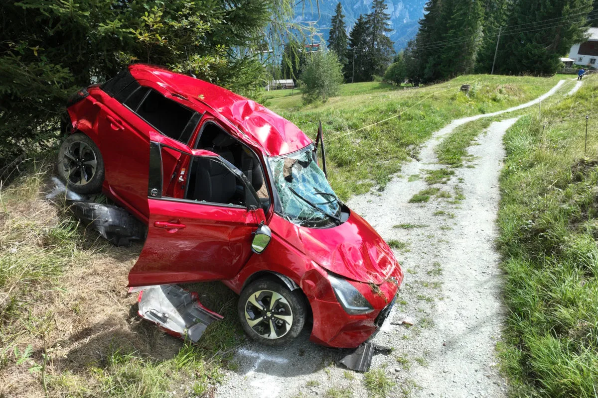 Ein rotes Auto ist von der schmalen, kurvigen Straße abgekommen und liegt mit starken Schäden im Gras.