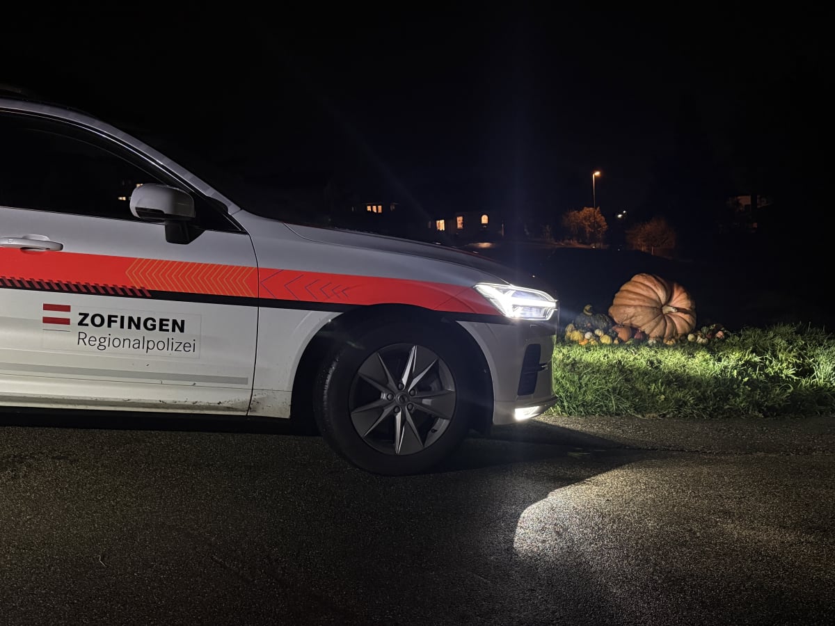 Ein Polizeiauto der Regionalpolizei Zofingen parkt nachts auf einer Straße, daneben steht ein großer beleuchteter Kürbis.