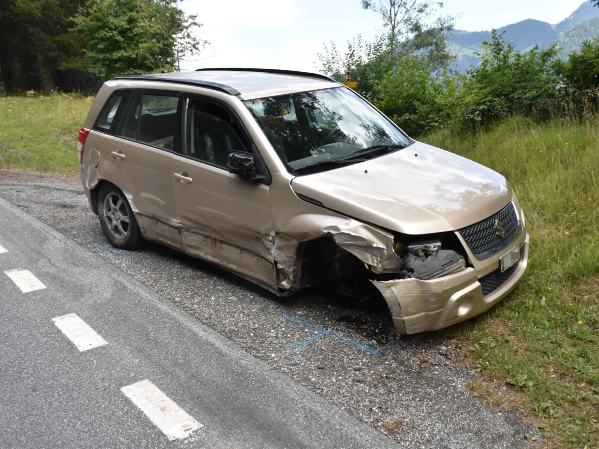 Ein bordeauxfarbenes SUV steht am Straßenrand mit erheblichen Schäden an der rechten Frontseite und den Kotflügeln. Die Umgebung ist grün und ländlich.