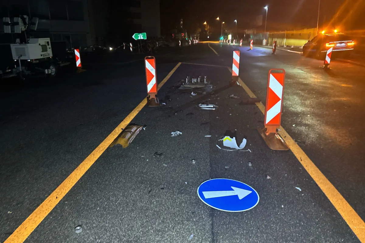 Auf einer nächtlichen Straße liegen beschädigte Verkehrsschilder und Absperrungen samt Trümmerteilen verteilt. Ein Fahrzeug mit Warnblinklicht steht in der Ferne.