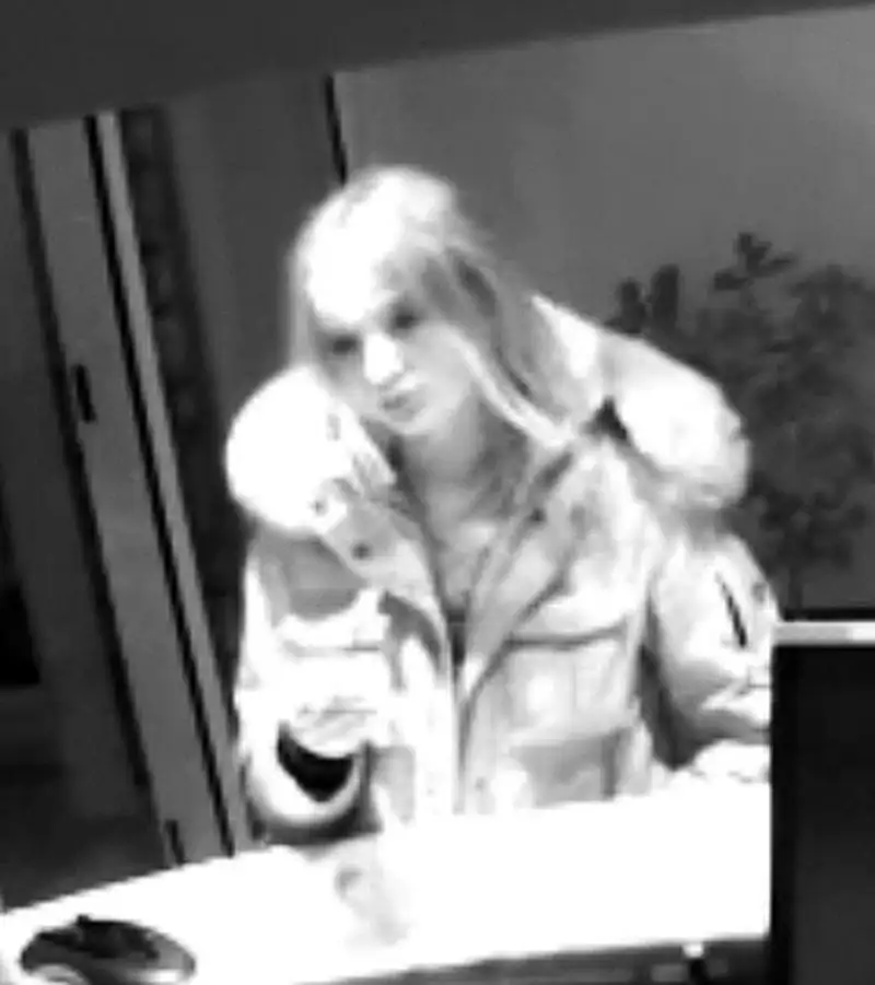 Eine Person in einem hellen Mantel steht an einem Tresen. Die Szene wirkt durch die Schwarz-Weiß-Aufnahme gedämpft.