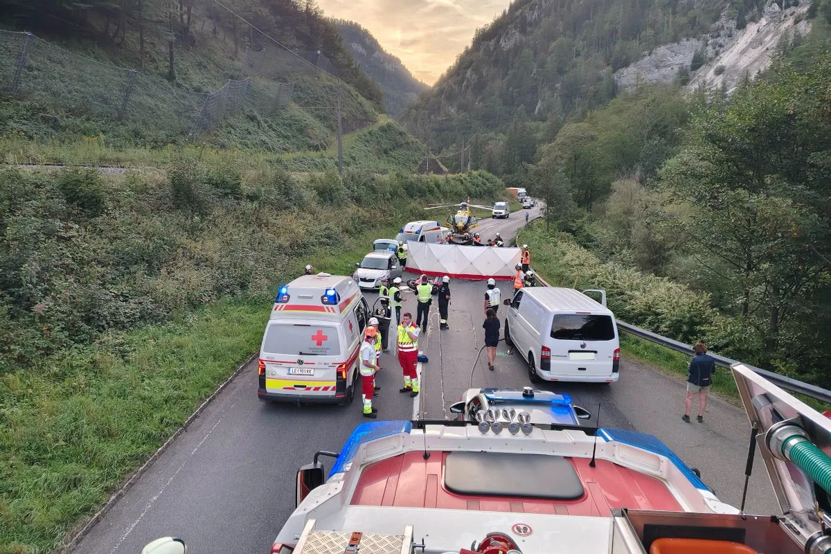Auf einer Bergstraße sind Rettungskräfte und ein Hubschrauber im Einsatz. Fahrzeuge der Rettungsdienste blockieren die Straße.