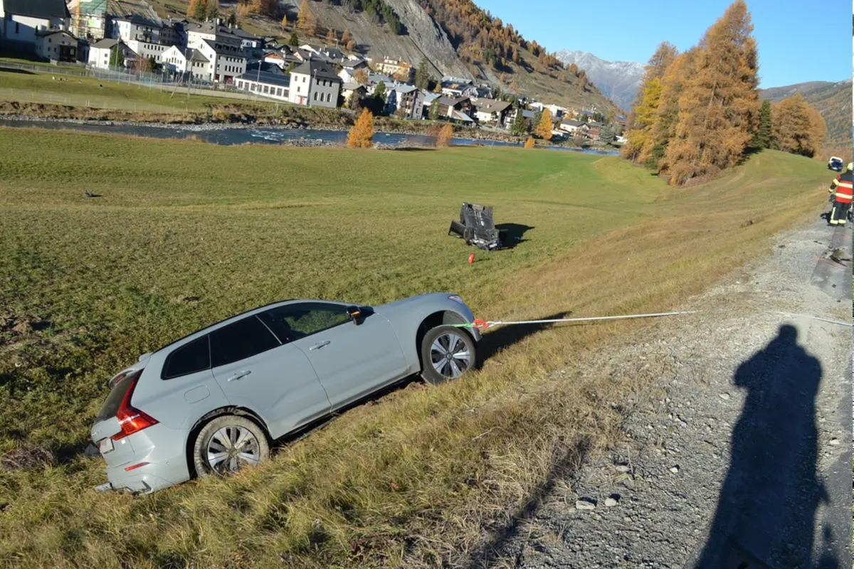 Ein silberfarbenes Auto wird mit einem Seil aus einem steilen Hang gezogen. Im Hintergrund sind eine Ortschaft und Berge zu sehen.