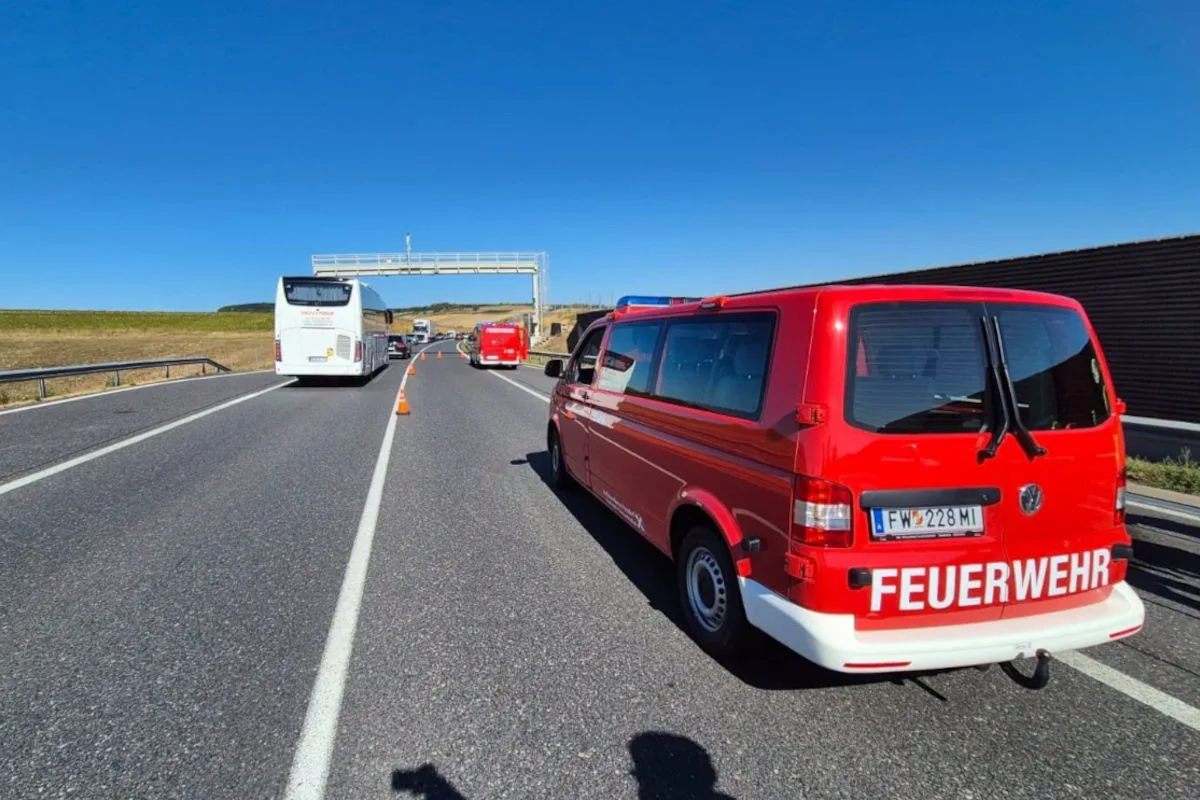 Ein rotes Feuerwehrfahrzeug und ein Reisebus stehen auf einer Autobahn. Verkehrshütchen sperren einen Bereich ab.