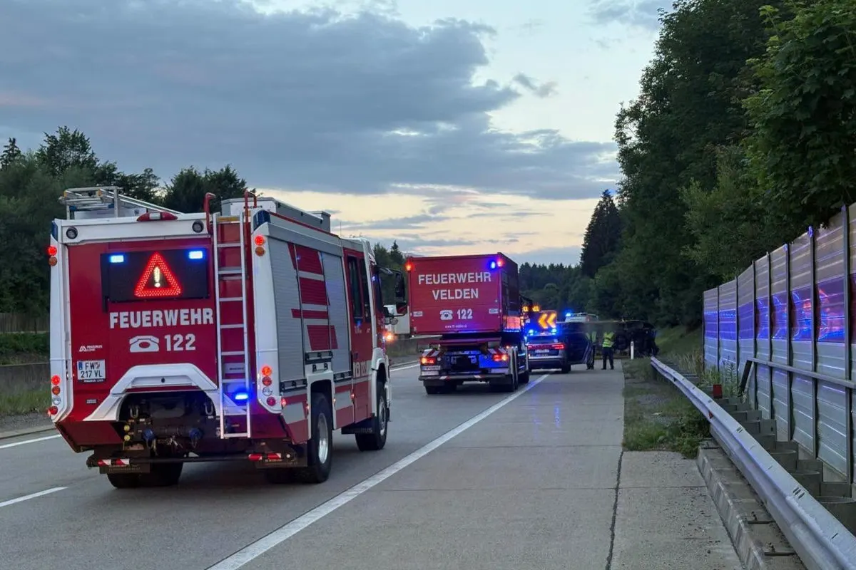 Zwei Feuerwehrfahrzeuge mit eingeschalteten Warnlichtern stehen auf einer Autobahn. Im Hintergrund sind weitere Einsatzfahrzeuge und Personen erkennbar.