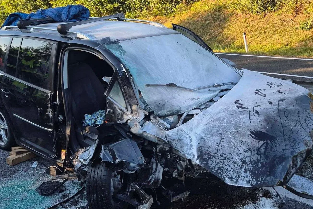 Ein Auto mit schwer beschädigter Vorderfront steht am Straßenrand. Die Motorhaube ist stark eingedellt und Teile liegen herum.