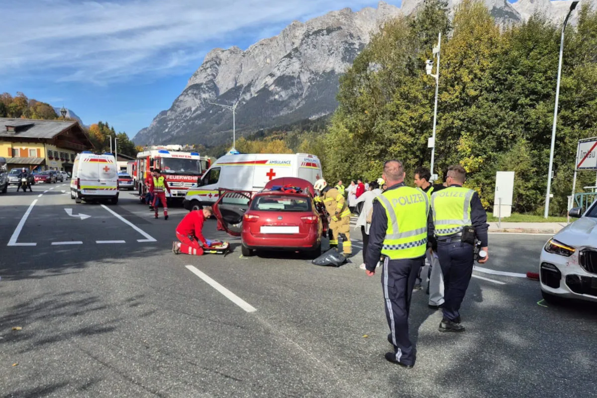 Rettungskräfte arbeiten an einer Unfallstelle auf einer Straße mit einem roten Auto, Polizei und Fahrzeuge des Rettungsdienstes sind anwesend.