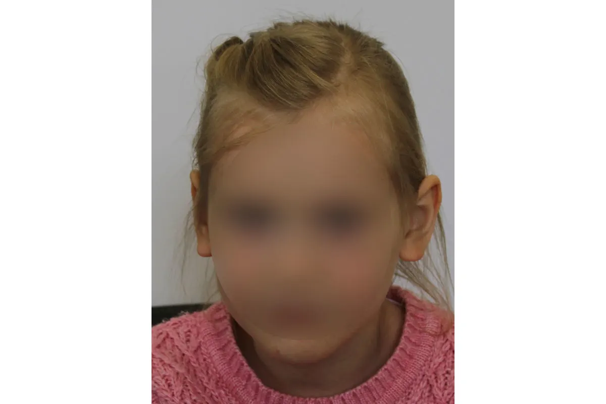 Ein Kind mit einem pinken Pullover ist in die Kamera gerichtet. Das Gesicht ist unkenntlich gemacht.