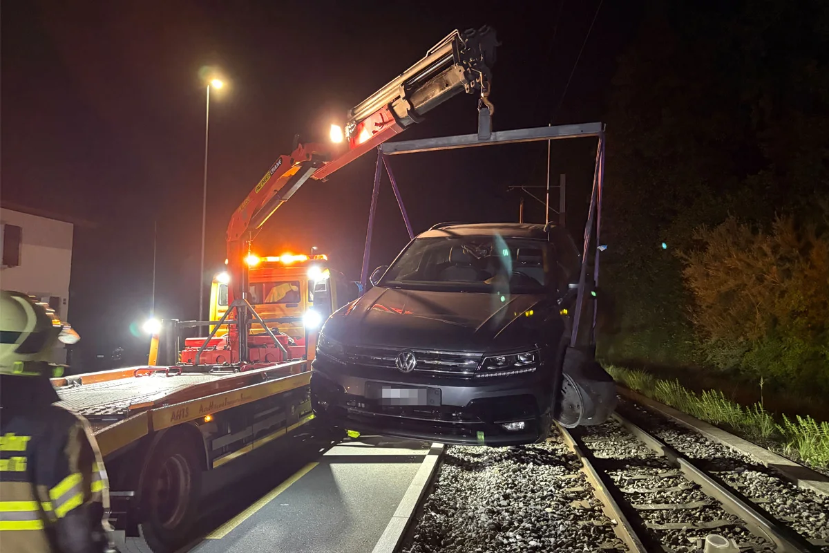 Ein Abschleppfahrzeug hebt nachts einen schwarzen VW von Bahngleisen. Einsatzkräfte sind vor Ort.