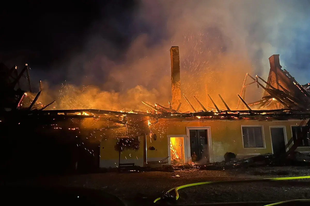 Ein Wohnhaus brennt bei Nacht; Flammen und Rauch steigen aus dem stark beschädigten Dach hervor.