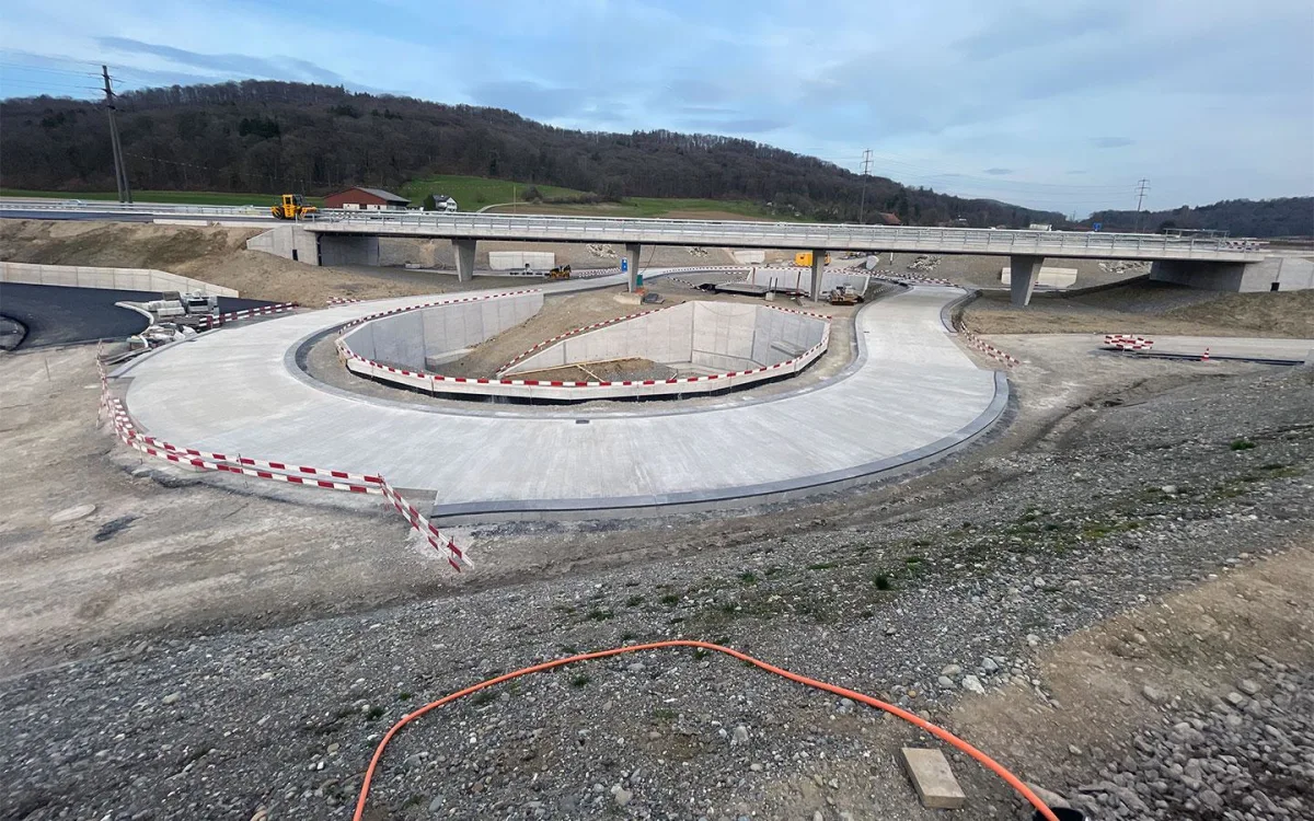 Das Bild zeigt einen neu gebauten Kreisverkehr unter einer Brücke in einem ländlichen Gebiet. Baustellenabsperrungen sind sichtbar.